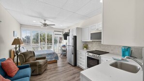 A modern kitchen with white cabinets, a stove, and a sink. There is a dining area with a table and chairs, and a balcony with a view. - Amazing Studio on Intracoastal Water Just Across from the Beach (Indian Shores)