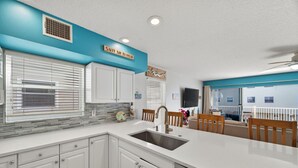 A modern kitchen with white cabinets, a stainless steel sink, and a Bosch dishwasher. There is a sign above the sink that reads "SALTY AIR REFRESH." - 🌅 Captain’s Cove 402 | 2BR Condo Across from Indian Shores Beach (Indian Shores)