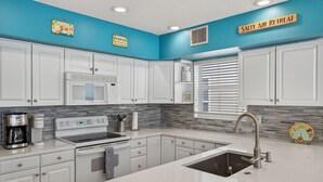 A modern kitchen with white cabinets, a stainless steel sink, and a blue accent wall. - 🌅 Captain’s Cove 402 | 2BR Condo Across from Indian Shores Beach (Indian Shores)