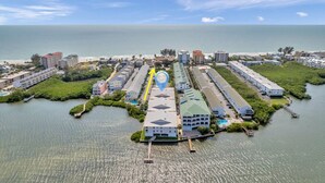 An aerial view of a coastal resort with multiple buildings, a marina, and a clear view of the ocean. - 🌅 Captain’s Cove 402 | 2BR Condo Across from Indian Shores Beach (Indian Shores)