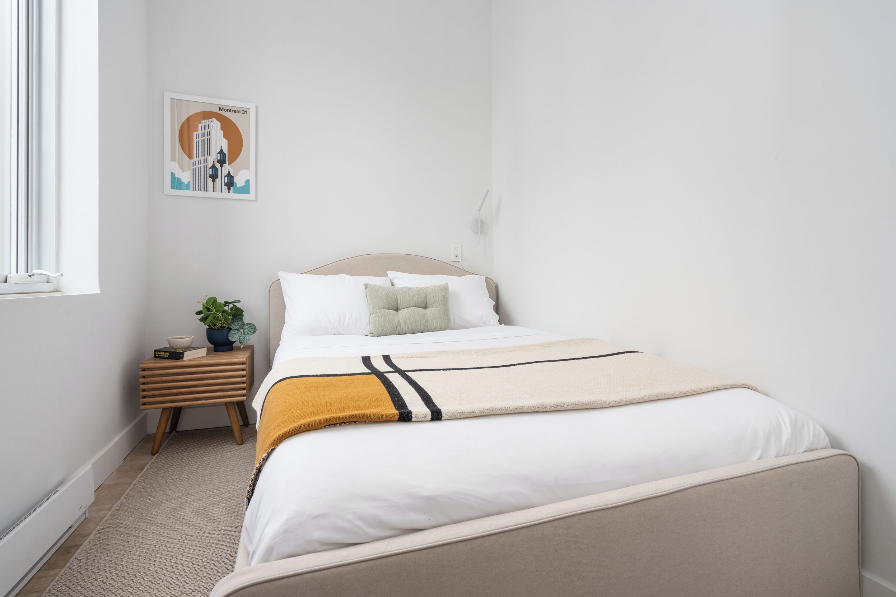 Un dormitorio ordenado con cama, mesita de noche e imagen colgada en la pared.
