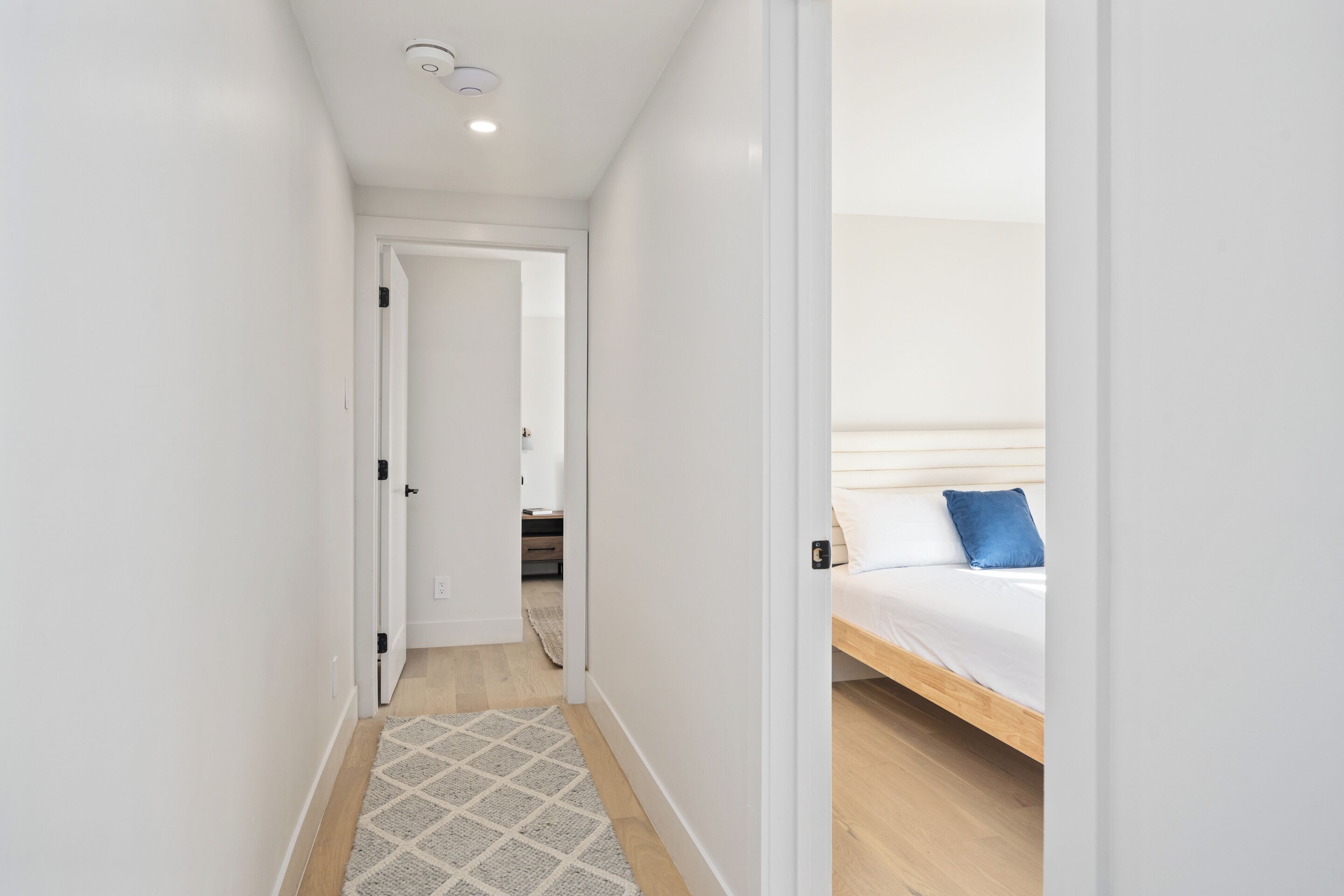 A narrow hallway leading to a bedroom with a bed and a blue pillow.