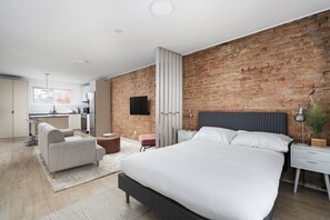 A modern bedroom with a large bed, a grey headboard, a bedside table, and a TV mounted on the brick wall.