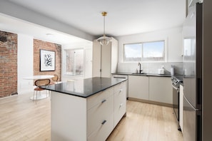 A modern kitchen with a central island, white cabinetry, a hanging light fixture, and a brick accent wall. - MTL Central Stay Apartments (Montréal)
