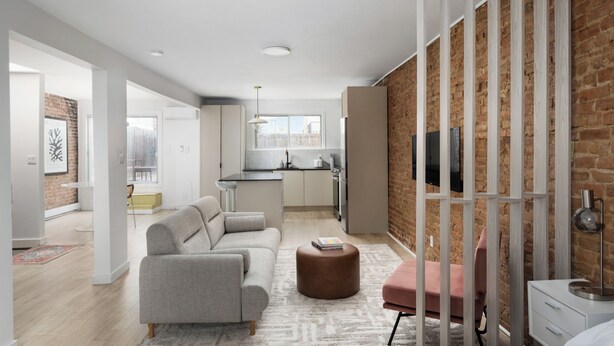 A modern apartment with a living area, kitchen, and a brick wall. - MTL Central Stay Apartments (Montréal)