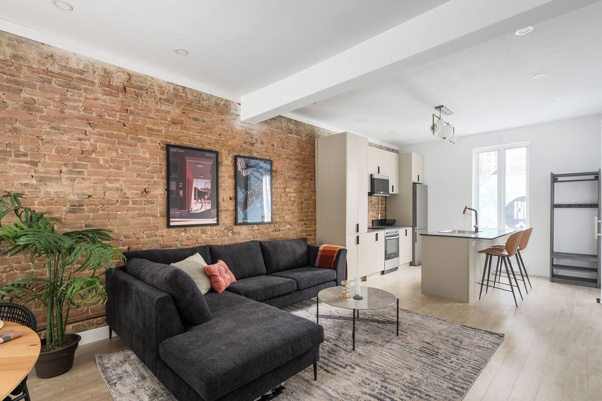 A modern living room with a brick wall, a dark grey sofa, a small coffee table, and a potted plant.