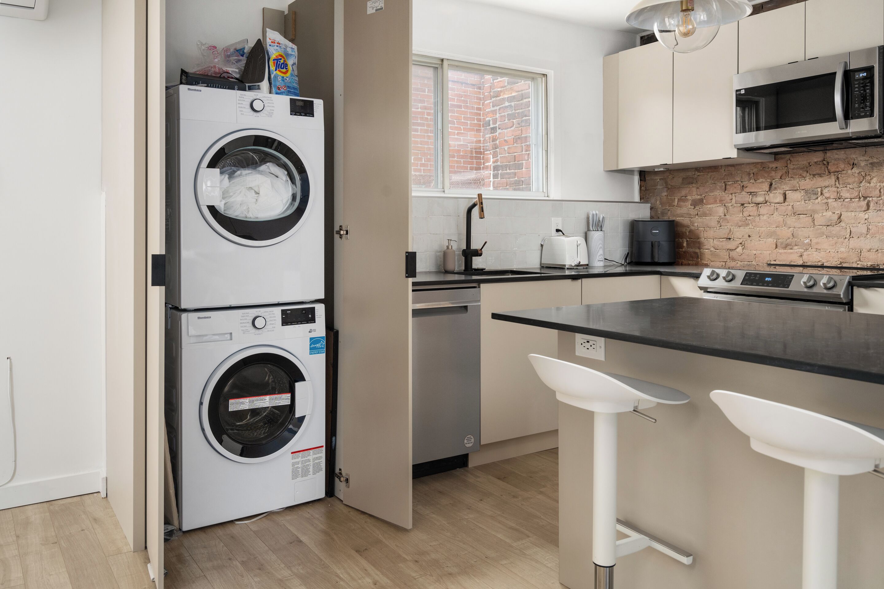 A compact kitchen with a washing machine, a dishwasher, a microwave, and a bar stool.