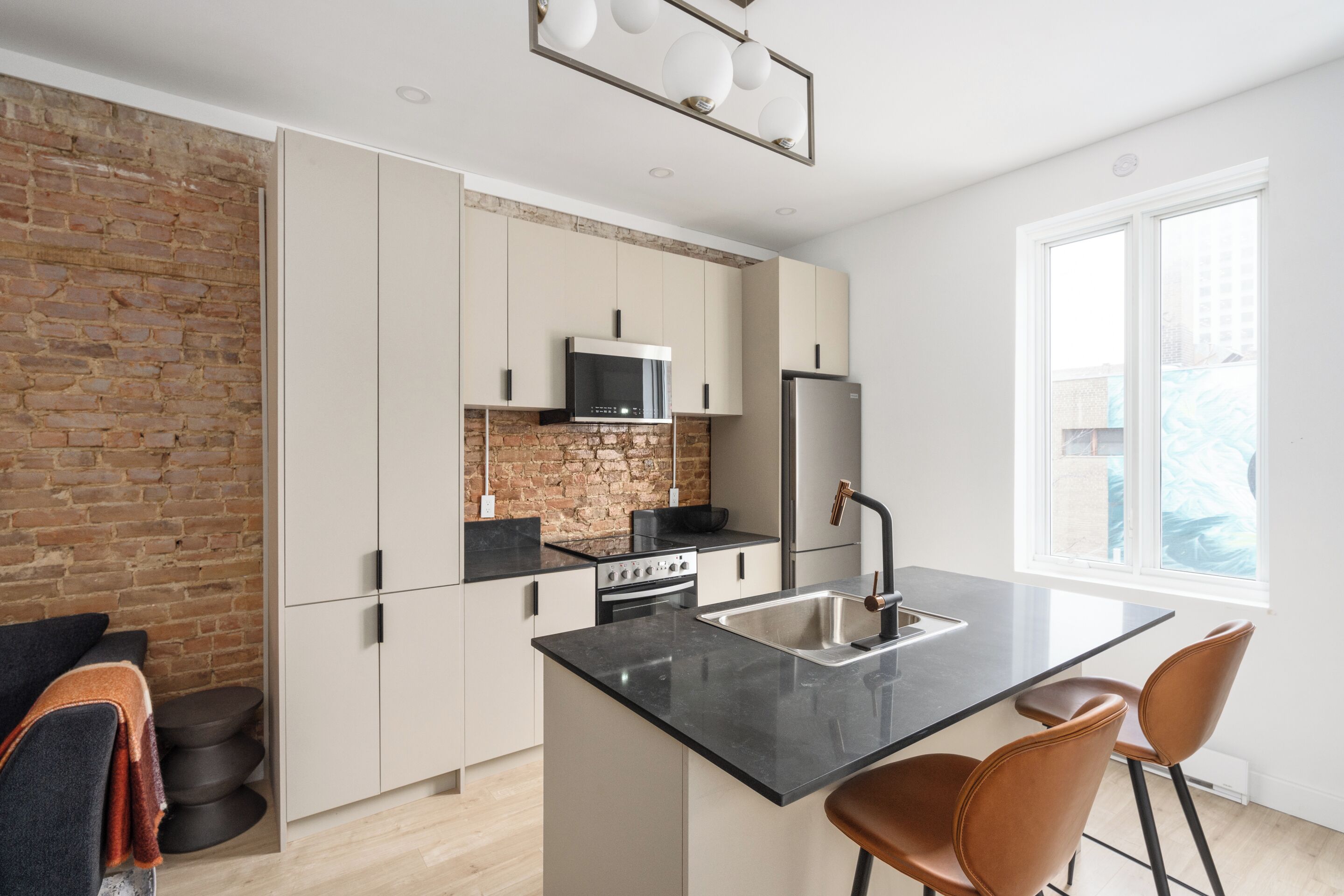 Una cocina moderna con pared de ladrillo, armarios blancos, encimera negra y pileta de acero inoxidable.