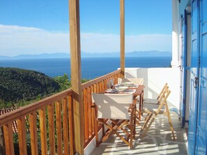 Un balcon avec une table dressée pour deux personnes, offrant une vue sur un paysage montagneux et la mer.