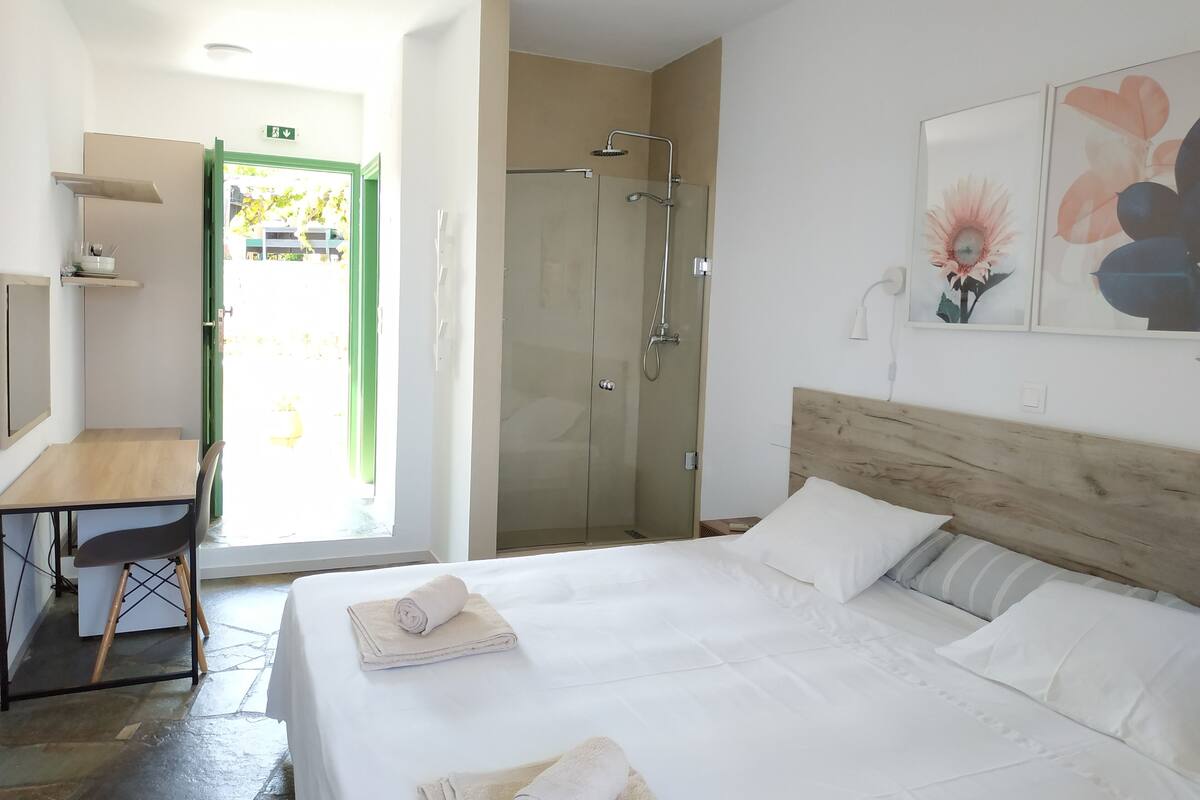 Una camera d'albergo con un letto, una scrivania, una doccia e una porta che dà sull'esterno.