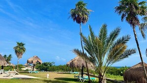 Ein tropisches Resort mit strohgedeckten Hütten, Palmen und Liegestühlen.