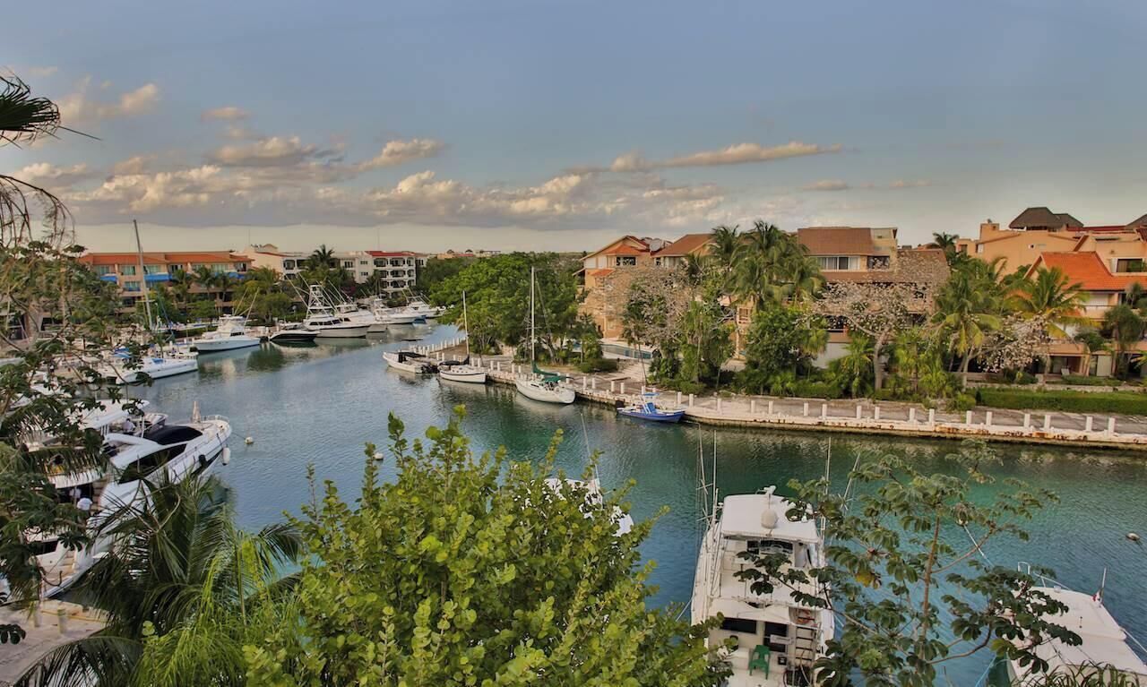 A marina with boats docked, surrounded by buildings and greenery.