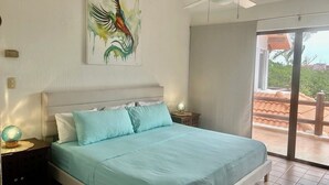 Ein Schlafzimmer mit Bett, Nachttisch, Globus, Deckenventilator, einem Bild und einer Glasschiebetür, die zu einem Außenbereich führt.