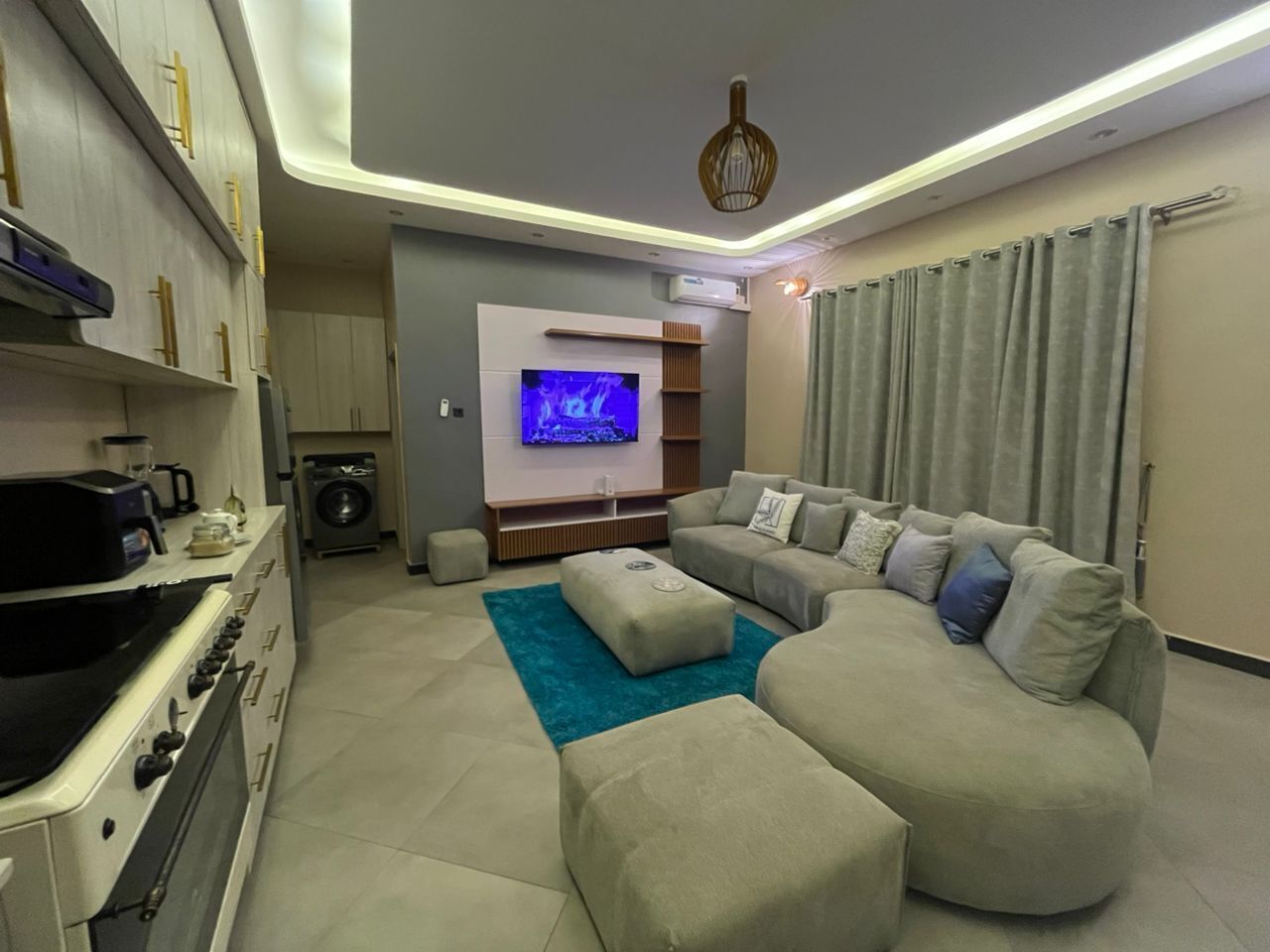 A modern living room with a sofa, ottoman, and a flat-screen TV mounted on the wall.