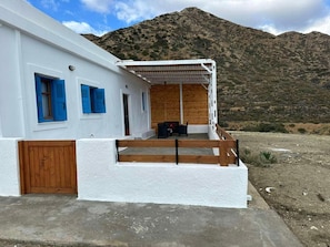 A white building with blue shutters, a wooden door, and a balcony with a table and chairs.