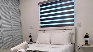 Un dormitorio moderno con cama, mesita de noche, ventana con persianas y ventilador de techo.