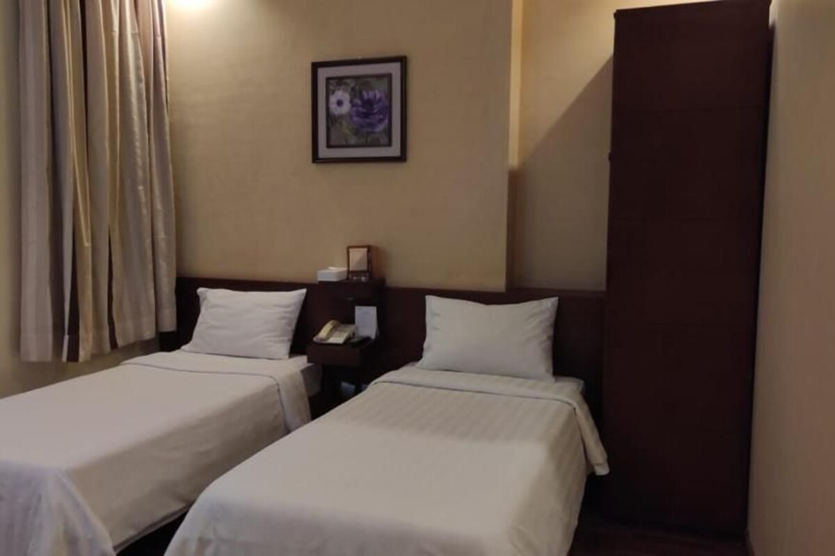 Habitación de hotel con dos camas individuales, una mesita de noche con teléfono, un cuadro en la pared y una ventana con cortinas.