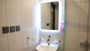 Un baño moderno con lavamanos blanco, un espejo y una cabina de ducha con mampara de vidrio.