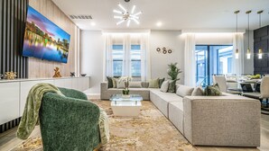 Een moderne woonkamer met een grote flatscreen-tv, een hoekbank, een glazen salontafel en een decoratieve plant.