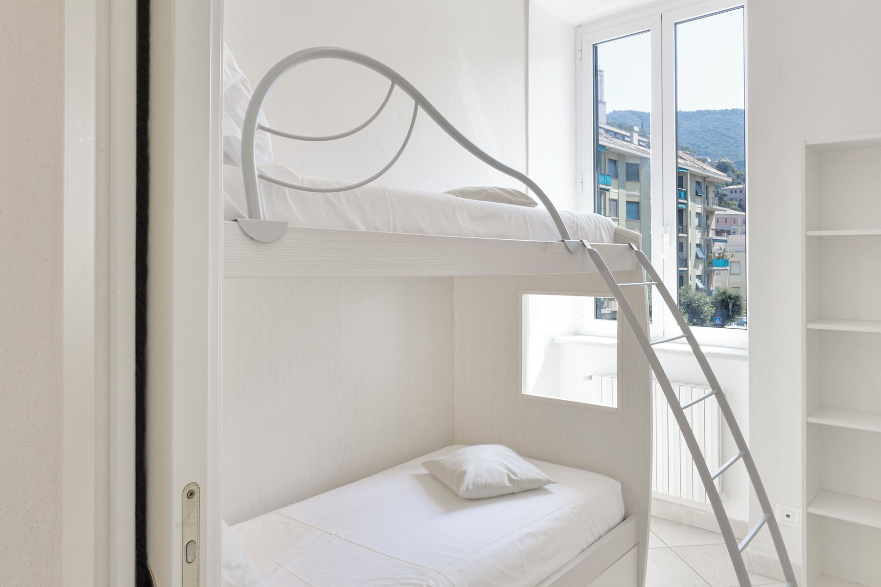 Un lit superposé avec une échelle, une petite fenêtre et un mur blanc.