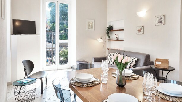 A modern living room with a dining area, large windows, and a flat-screen TV mounted on the wall. - Casa Vico delle Isole by Wonderful Italy (Recco)