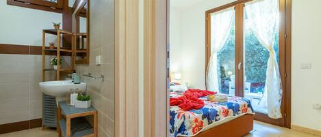 Ein Schlafzimmer mit Bett, Fenster, Badezimmer mit Waschbecken und Spiegel.