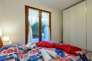 Ein Schlafzimmer mit Bett, Fenster mit Vorhängen, Nachttischlampe und Kleiderschrank.