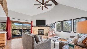 A spacious living room with a fireplace, a television, and a balcony with red curtains. - Condo with Ski Locker | Peak Views (Breckenridge)