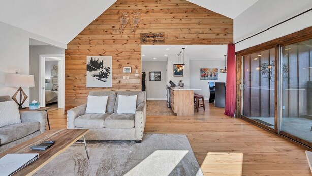 A modern living room with a wooden ceiling, a sofa, a coffee table, and a kitchen area visible through an open doorway. - Condo with Ski Locker | Peak Views (Breckenridge)