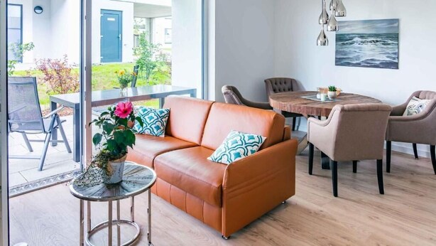 Ein modernes Wohnzimmer mit einer Ledersofa, einem runden Esstisch und Blick ins Freie.