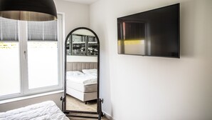 Ein Schlafzimmer mit Bett, einem großen Spiegel, einem an der Wand montierten Fernseher und einem Fenster mit Jalousien.
