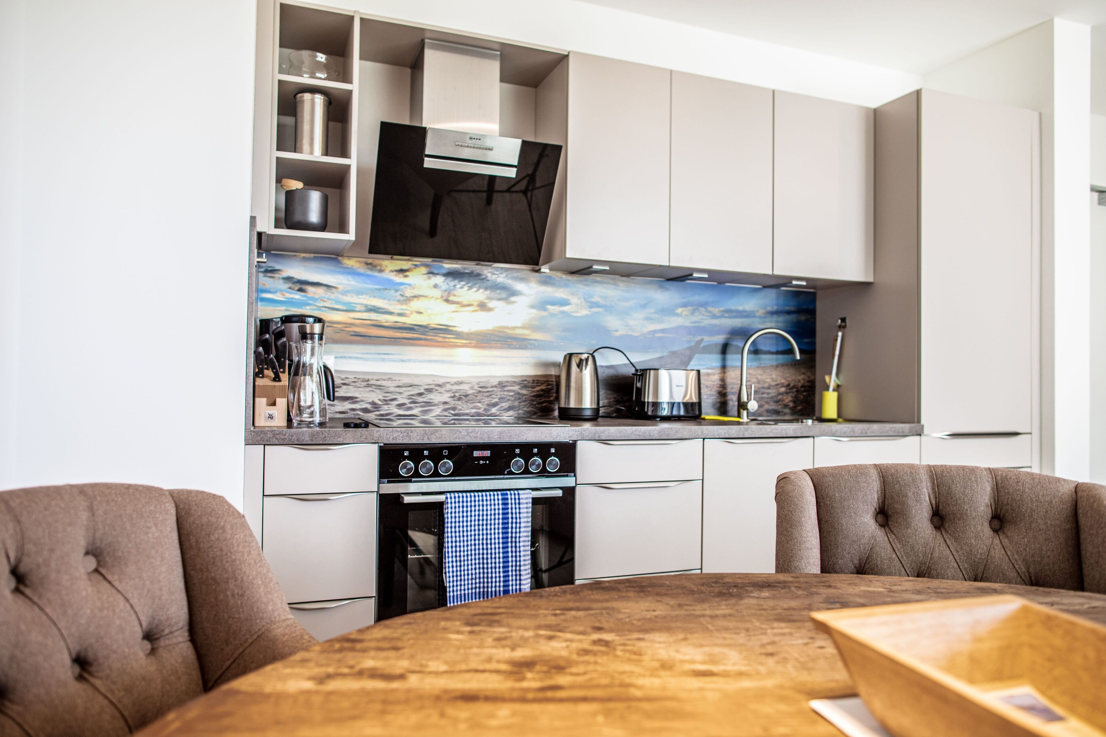 A modern kitchen with a built-in oven, a coffee maker, and a kettle on the countertop.