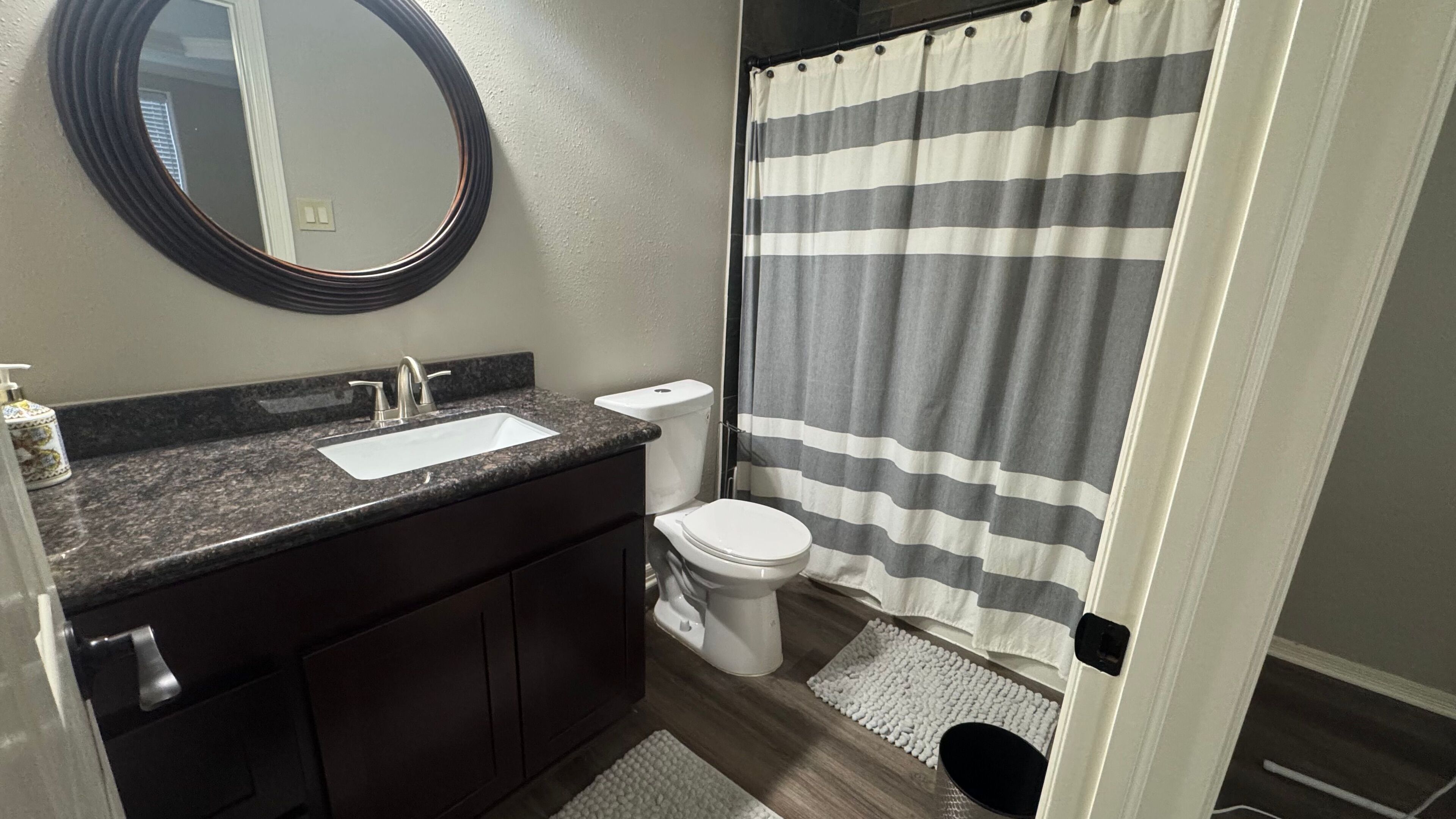 Bathroom featuring a dark vanity, oval mirror, and striped shower curtain.