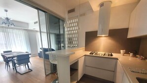 Una cucina moderna con piano cottura integrato, zona pranzo con tavolo e sedie, e una porta scorrevole in vetro che dà su un soggiorno.