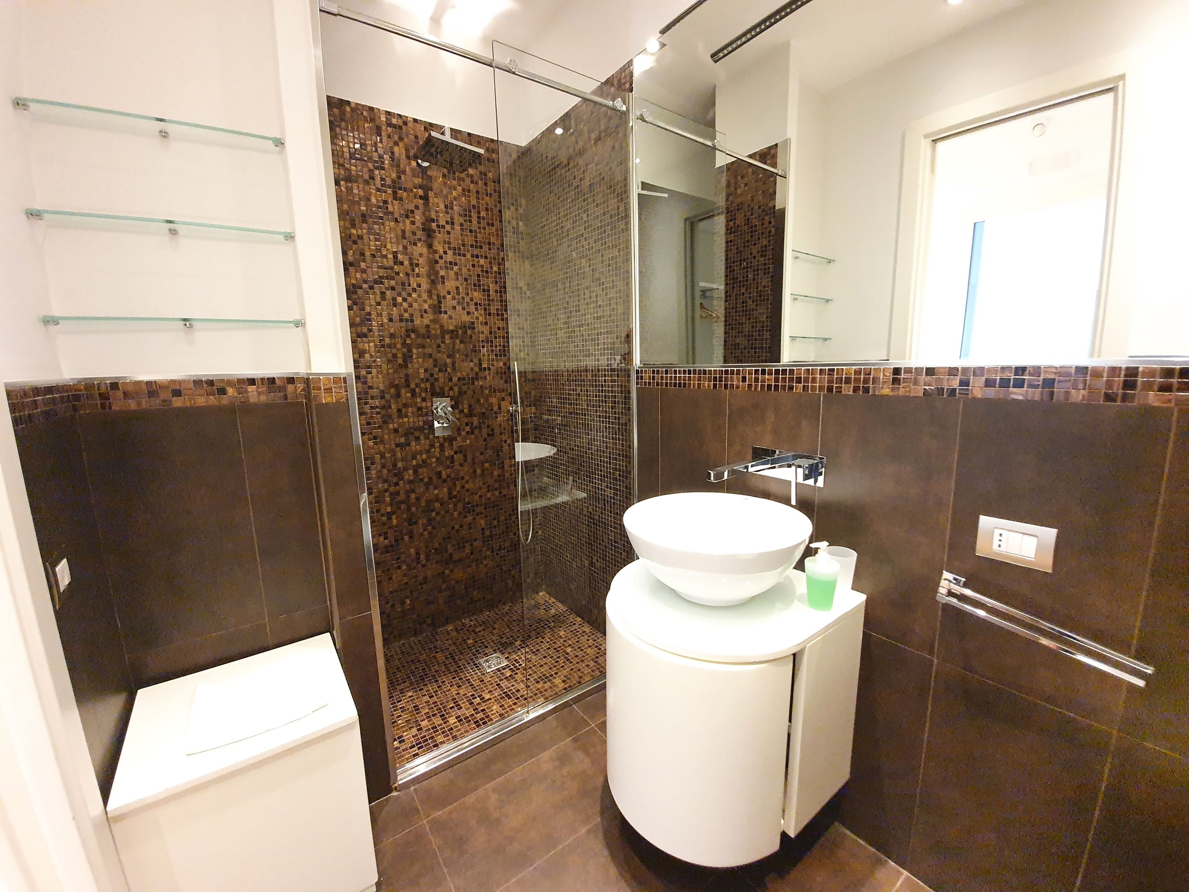 Un bagno moderno con doccia vetrata, lavandino bianco e specchio sopra.