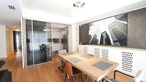 Un appartamento moderno con zona pranzo, tavolo e sedie in legno, cucina con frigorifero e un'ampia finestra vista sulla città.