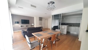 Un soggiorno moderno con zona pranzo, divano, televisore e cucina sullo sfondo.
