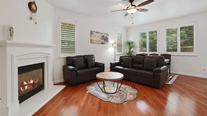 A living room with two dark leather sofas, a round wooden coffee table, a fireplace, and a ceiling fan. - Spacious 4BR/4BA Tracy Home for Families & Groups! (Tracy)