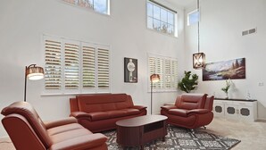 A modern living room with a brown leather sofa, a matching armchair, and a coffee table. There are two floor lamps, a painting on the wall, and a cabinet with decorative items. - Spacious 4BR/4BA Tracy Home for Families & Groups! (Tracy)