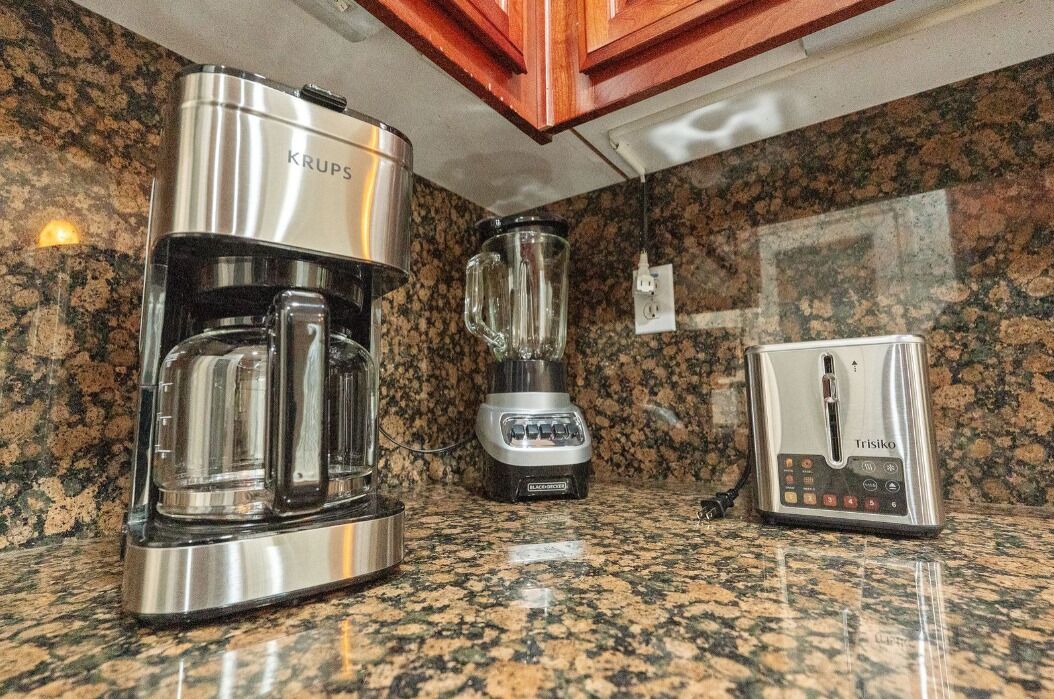 A kitchen with a Krups coffee maker, a blender, and a Trisiko scale on a granite countertop.