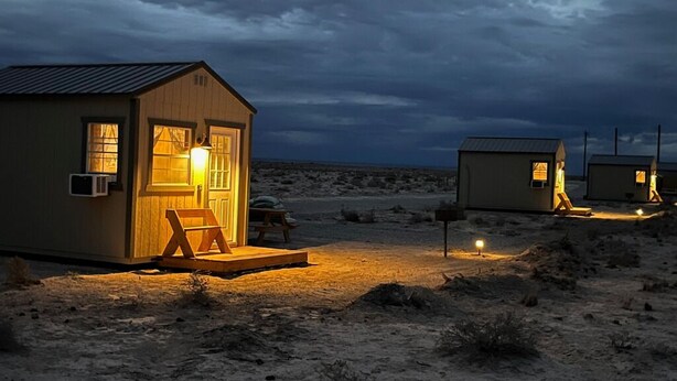 Une rangée de petites cabanes à un seul étage, avec une façade en bois, chacune dotée d'un porche à l'avant et d'une seule fenêtre.