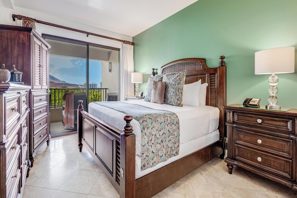 Een ruime slaapkamer met een groot bed, een houten dressoir, een nachtkastje en een balkon met uitzicht.