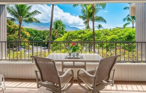 Un balcón con mesa y sillas, con vistas a un paisaje tropical de palmeras y cielo despejado.