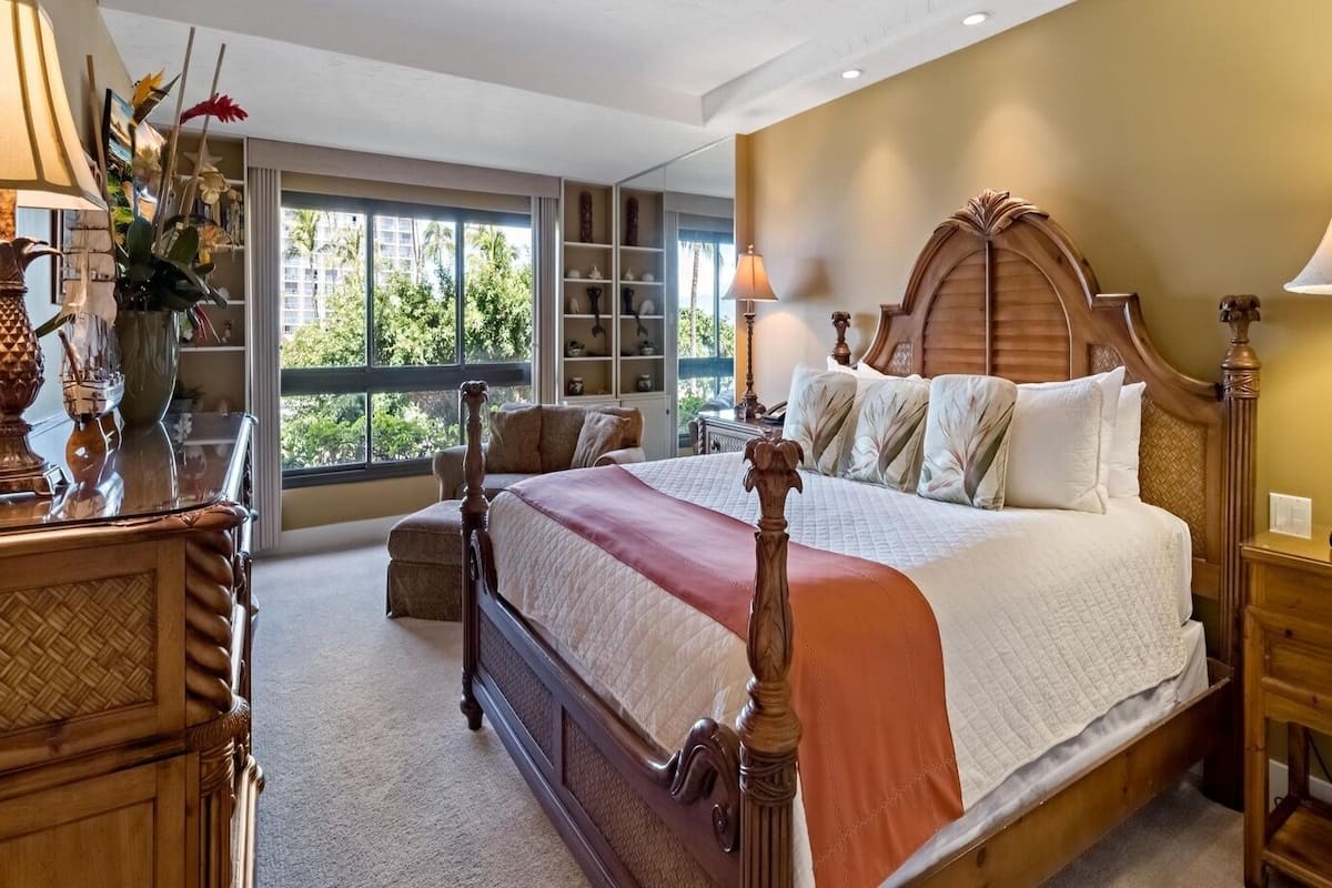 Een ruime slaapkamer met een groot bed, een houten hoofdbord, een nachtkastje en uitzicht op groen.