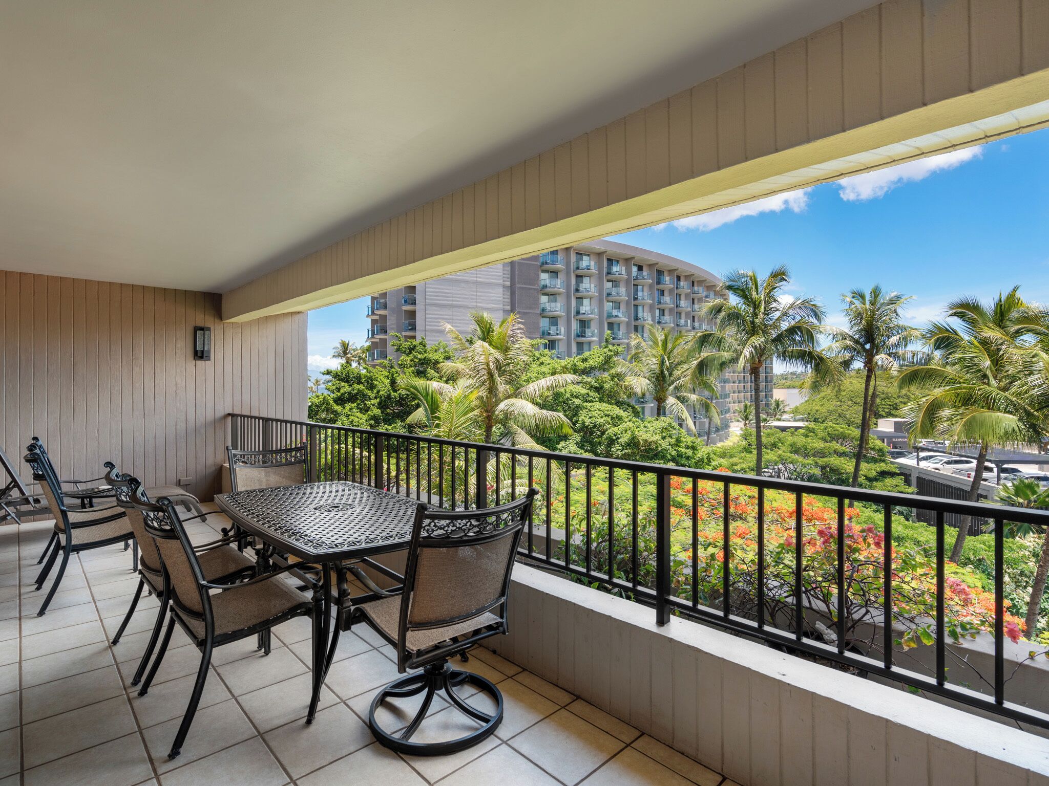 A balcony with a table and chairs, overlooking a lush garden and a high-rise building.