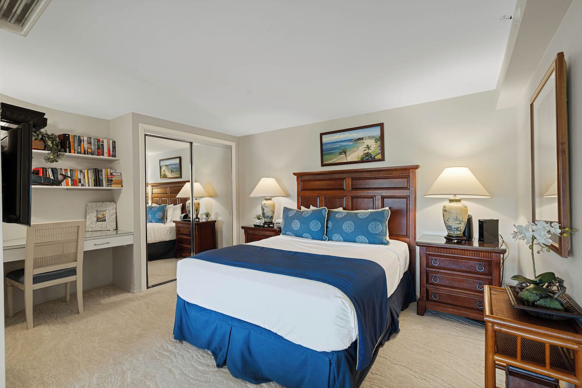 Een slaapkamer met een groot bed, nachtkastjes, een bureau, een boekenplank en een spiegel.