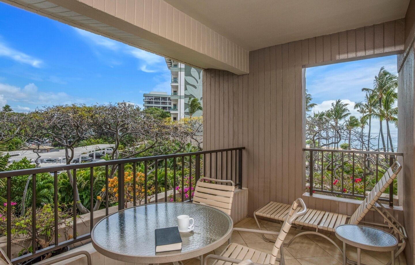A balcony with a glass table, a chair, a sofa, and a view of the cityscape and palm trees.