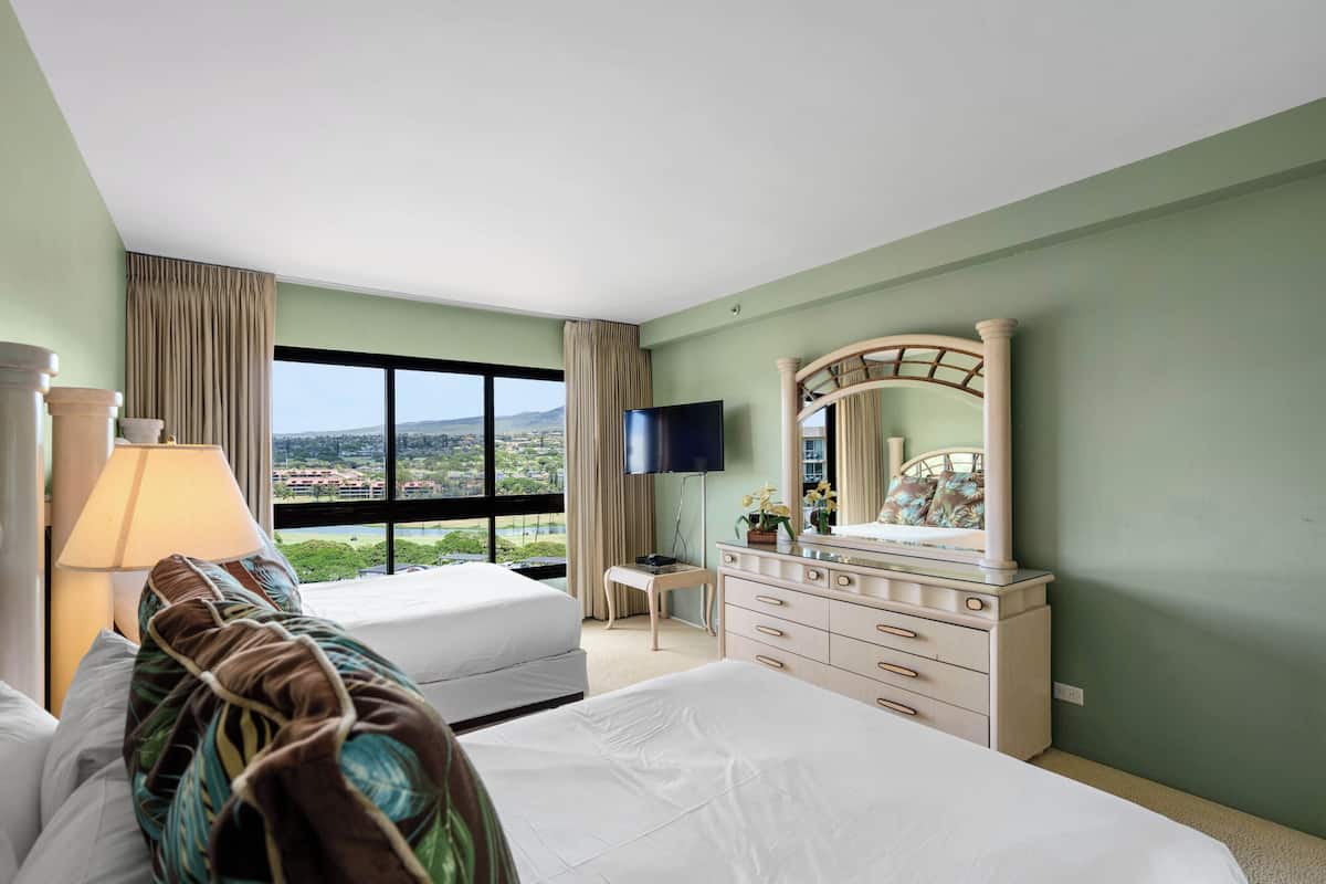 Een hotelkamer met een bed, een dressoir, een televisie en een groot raam met uitzicht op de stad.
