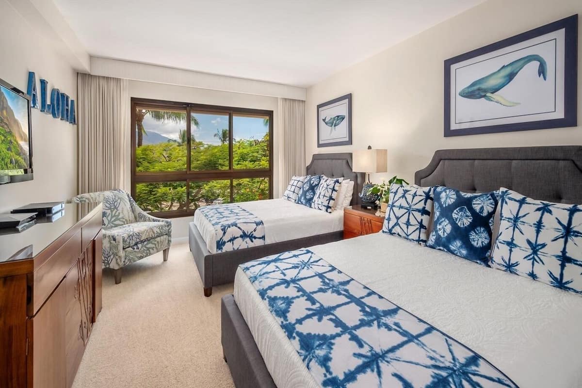 Une chambre d’hôtel avec deux lits, un bureau, une chaise, une télévision et de grandes fenêtres donnant sur un paysage verdoyant.