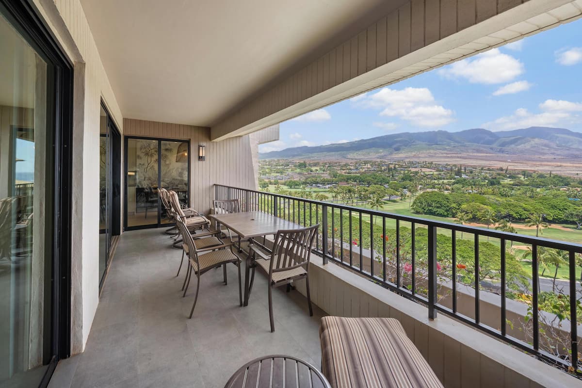 Een balkon met een eettafel en uitzicht op een groen landschap en bergen.
